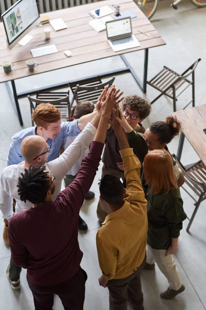 photo-of-people-holding-each-other-s-hands-3184433 A diverse group of professionals high-fiving in a modern office, showcasing teamwork and collaboration.
